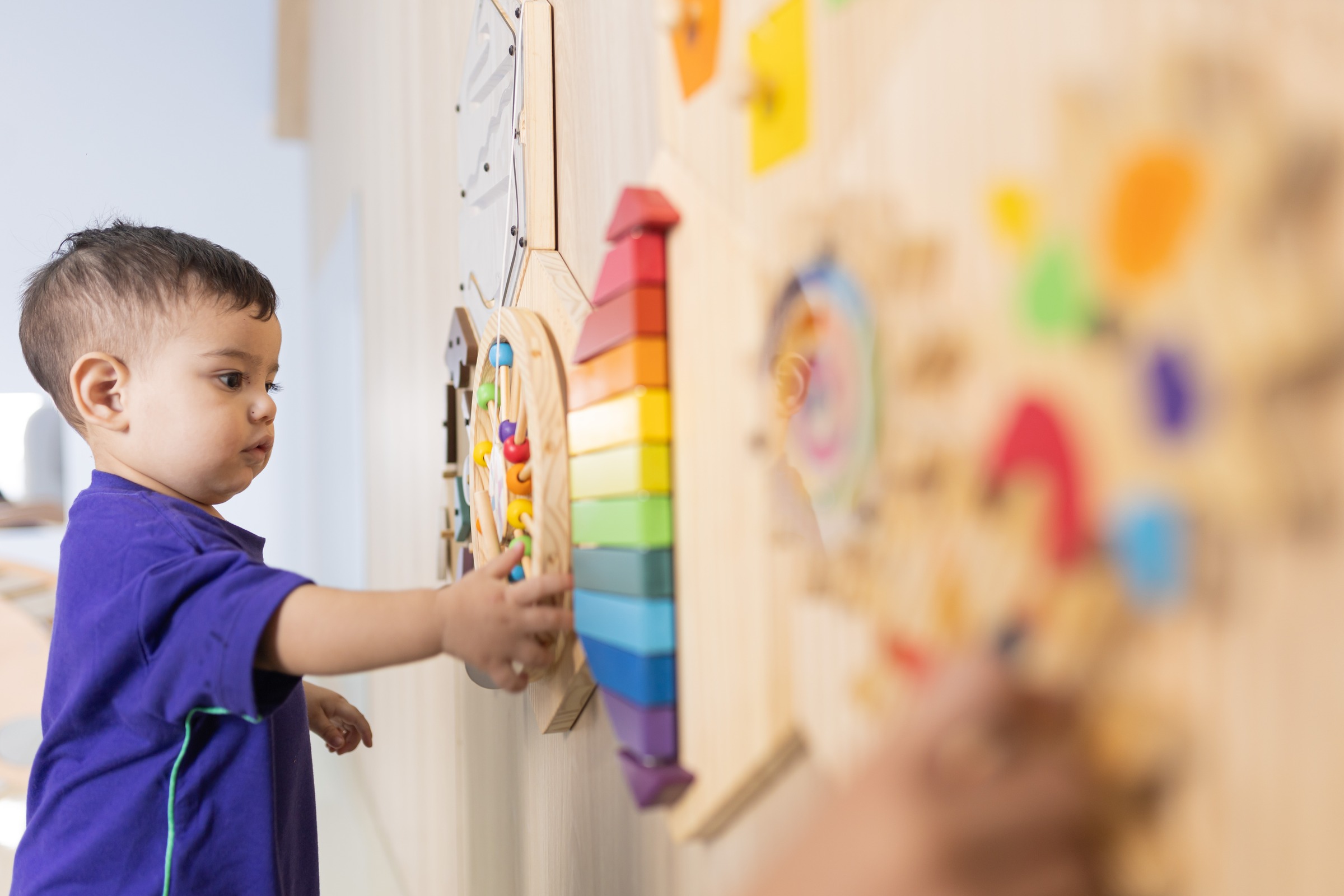 Criança da Cardim Kids explorando painel sensorial de madeira colorido fixado na parede