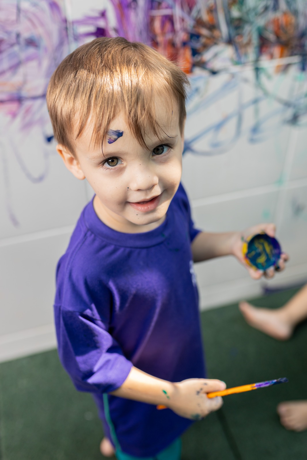 Menino da Cardim Kids com o rosto pintado, segurando pincel e tinta durante atividade de arte