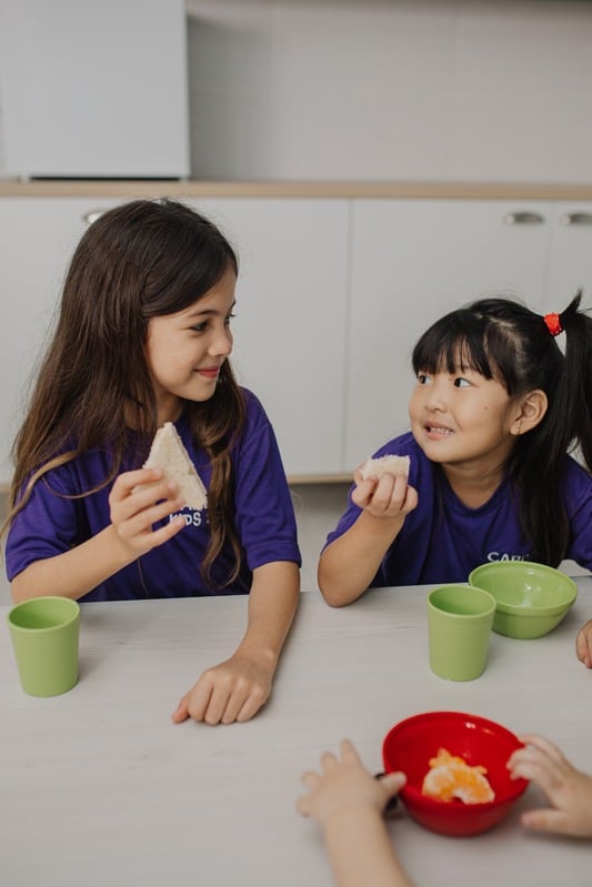 Duas meninas da Cardim Kids sentadas à mesa durante o lanche, conversando e sorrindo